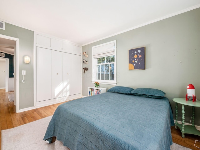 bedroom featuring a closet, visible vents, light wood-style flooring, ornamental molding, and baseboards