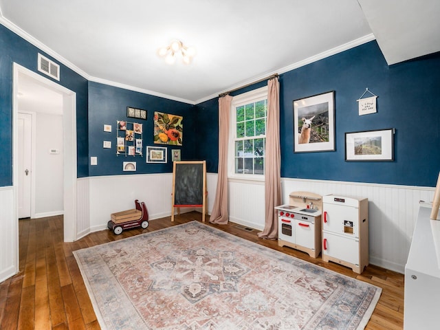 interior space featuring a wainscoted wall, wood-type flooring, visible vents, and ornamental molding