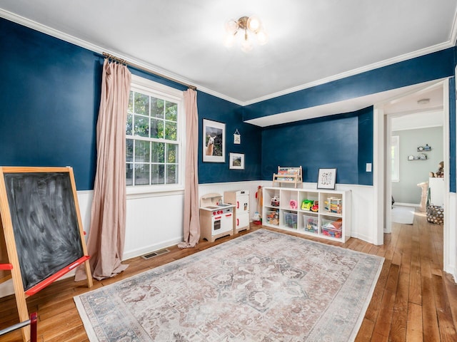 playroom featuring a wainscoted wall, ornamental molding, wood-type flooring, and visible vents