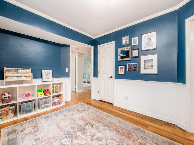 recreation room featuring crown molding, wood finished floors, and wainscoting