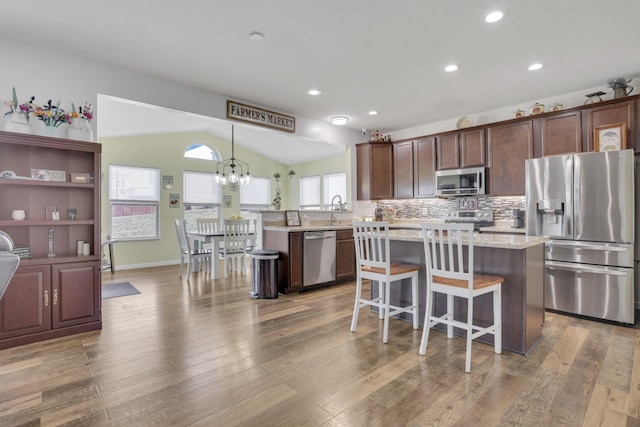 kitchen with light wood-type flooring, a kitchen island, appliances with stainless steel finishes, and vaulted ceiling