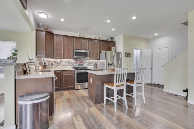 kitchen with a breakfast bar area, backsplash, appliances with stainless steel finishes, a sink, and a kitchen island