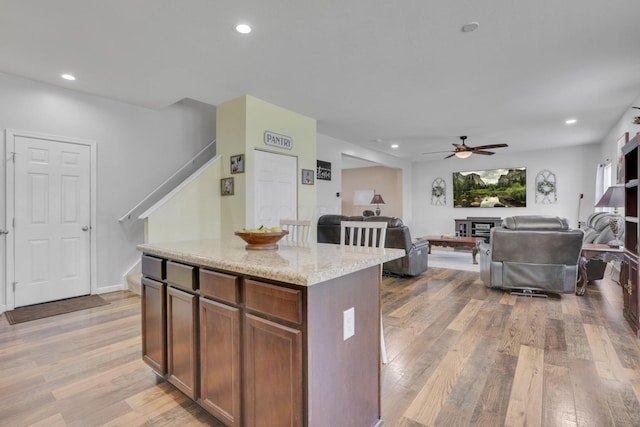 kitchen featuring light wood finished floors, recessed lighting, open floor plan, a kitchen island, and light stone countertops