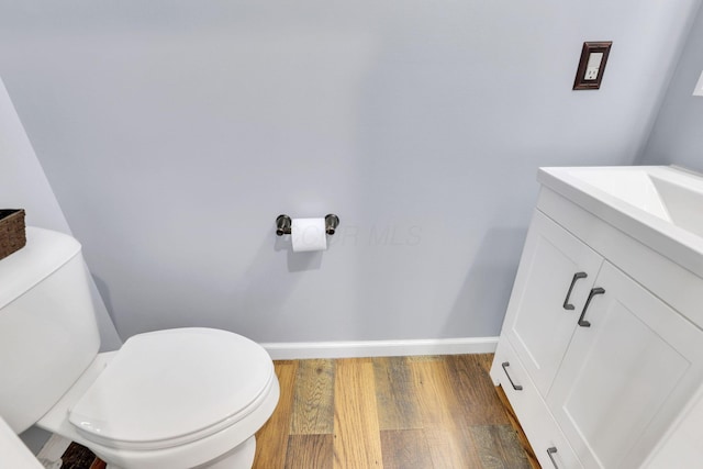 bathroom with toilet, baseboards, wood finished floors, and vanity