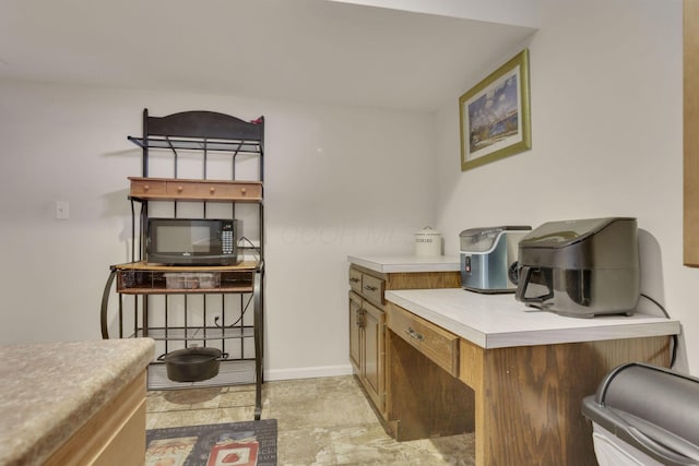 kitchen with brown cabinetry, baseboards, black microwave, and light countertops