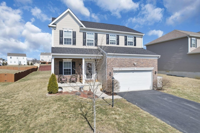 traditional home featuring brick siding, covered porch, a front yard, fence, and driveway