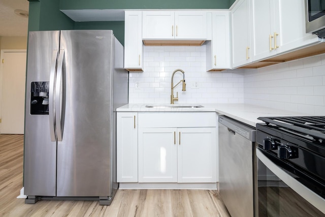 kitchen featuring appliances with stainless steel finishes, a sink, light wood-style floors, white cabinetry, and backsplash