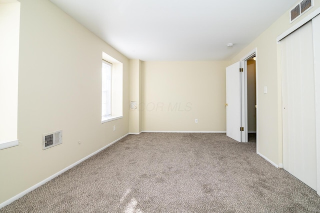 spare room featuring carpet floors, visible vents, and baseboards