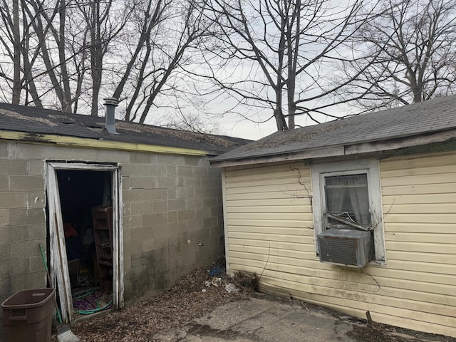 view of side of property with a shingled roof, an outbuilding, concrete block siding, and cooling unit