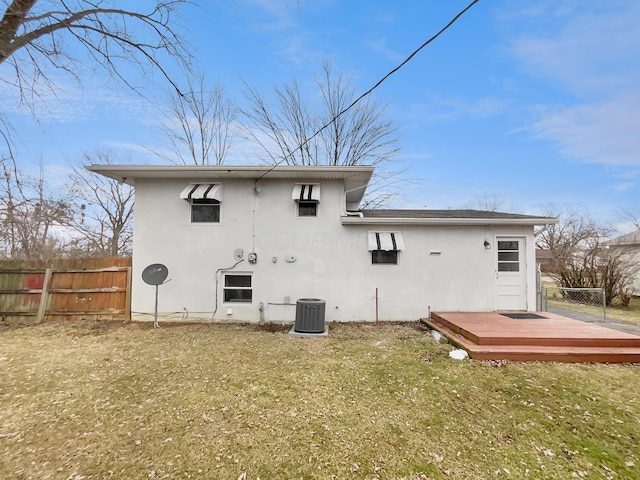 rear view of property featuring stucco siding, a lawn, central AC, fence, and a deck