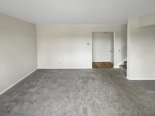 carpeted empty room featuring stairs and baseboards