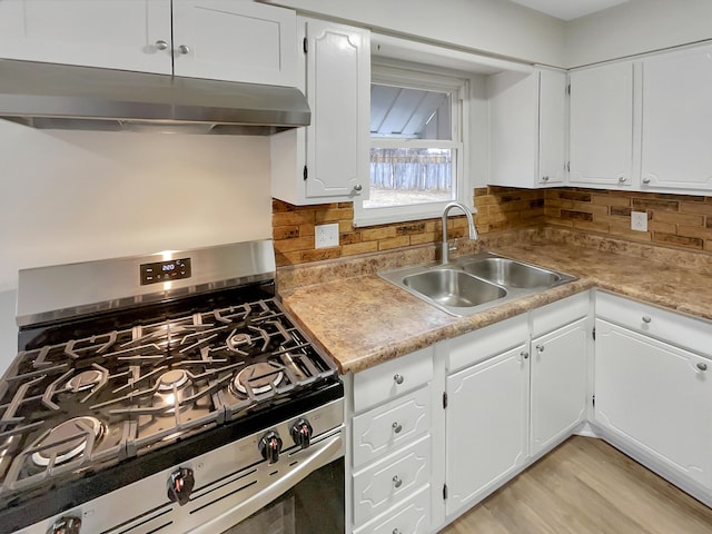 kitchen with stainless steel gas range oven, under cabinet range hood, a sink, white cabinetry, and decorative backsplash