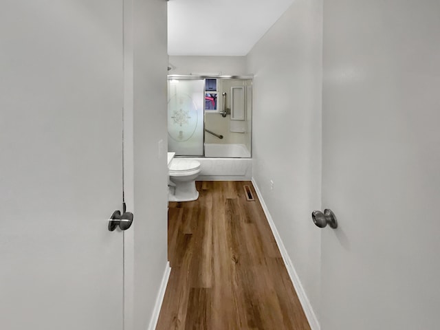 bathroom with visible vents, toilet, enclosed tub / shower combo, wood finished floors, and baseboards