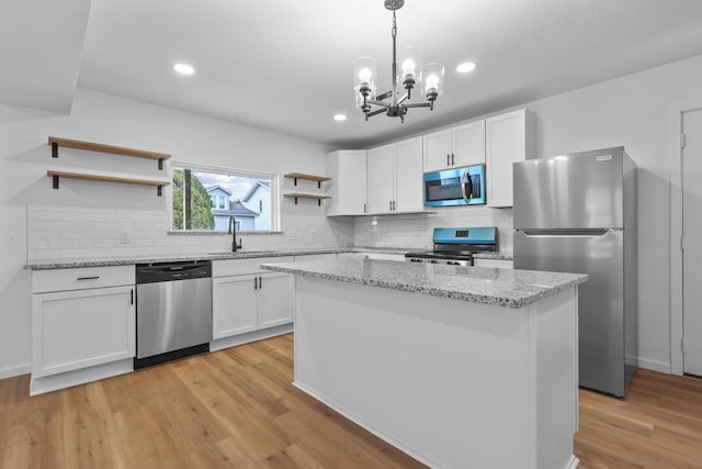 kitchen with light wood finished floors, white cabinets, stainless steel appliances, open shelves, and a sink