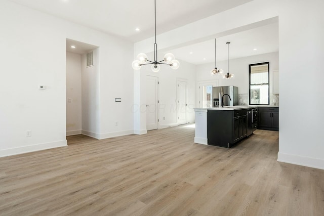 kitchen featuring light countertops, visible vents, light wood-style flooring, a kitchen island with sink, and stainless steel fridge with ice dispenser