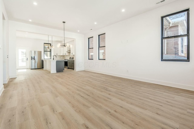 unfurnished living room featuring light wood-style flooring, a wealth of natural light, and baseboards