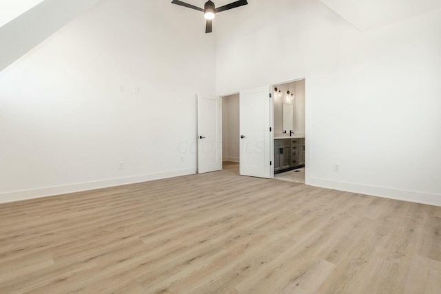 unfurnished bedroom featuring light wood-type flooring, high vaulted ceiling, baseboards, and ensuite bathroom