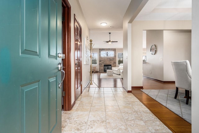 entryway with light wood-type flooring, ceiling fan, baseboards, and a stone fireplace