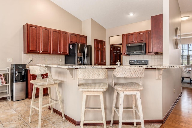 kitchen featuring stainless steel microwave, fridge with ice dispenser, a peninsula, and a kitchen breakfast bar