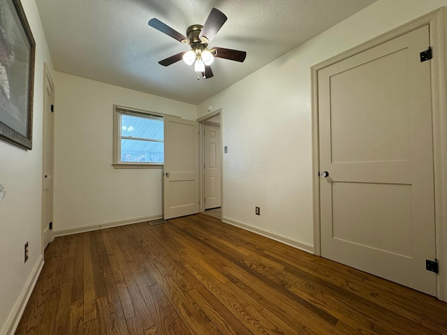 unfurnished bedroom featuring ceiling fan, a textured ceiling, baseboards, and wood finished floors