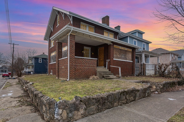 view of front of home featuring covered porch, brick siding, a chimney, and a lawn