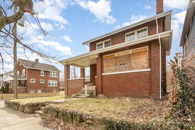 view of front of house featuring a chimney, a porch, and brick siding