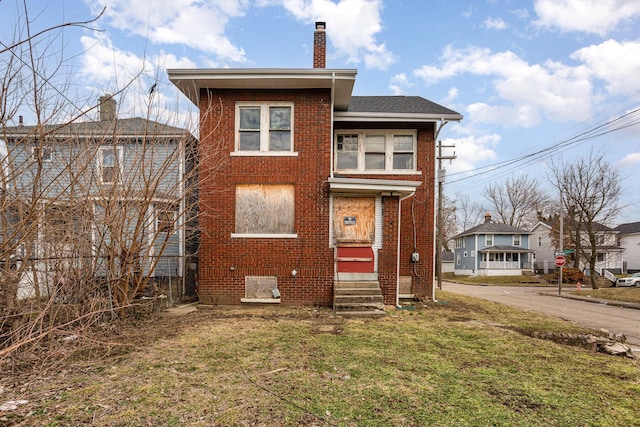 view of front facade with entry steps, brick siding, a shingled roof, a chimney, and a front yard