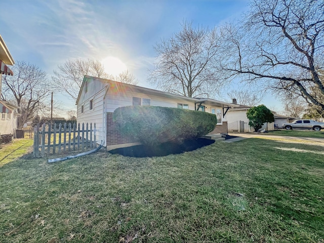 view of side of home featuring brick siding, a lawn, and fence