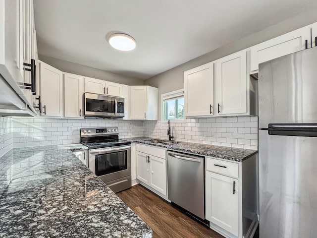 kitchen featuring dark wood finished floors, dark stone counters, stainless steel appliances, white cabinetry, and a sink