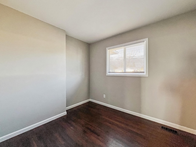 spare room with visible vents, baseboards, and dark wood finished floors