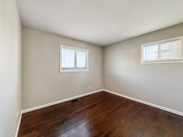 spare room featuring dark wood-type flooring, baseboards, visible vents, and a wealth of natural light