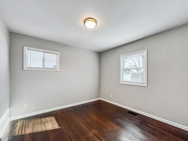 unfurnished room with visible vents, dark wood-type flooring, and a healthy amount of sunlight