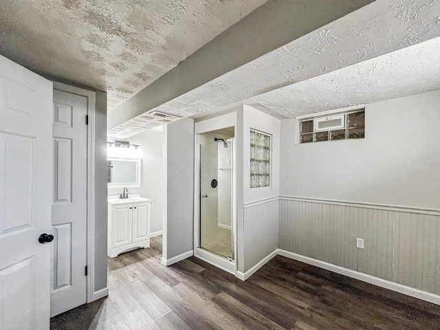 finished below grade area featuring baseboards, a wainscoted wall, wood finished floors, a textured ceiling, and a sink