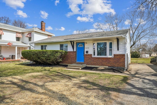 view of front of home with brick siding, a shingled roof, and a front yard