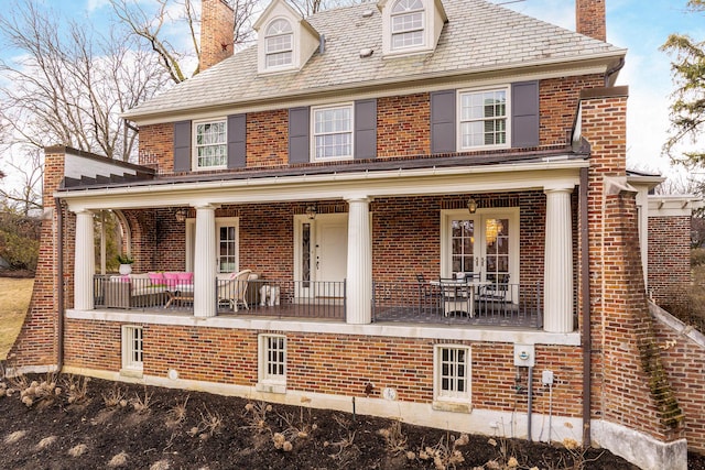 view of front of house featuring a chimney, french doors, a high end roof, a porch, and brick siding