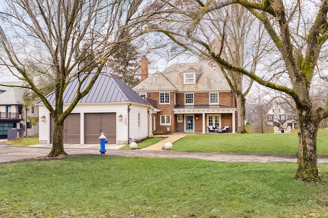 view of front of property with brick siding, a front yard, driveway, a standing seam roof, and a chimney