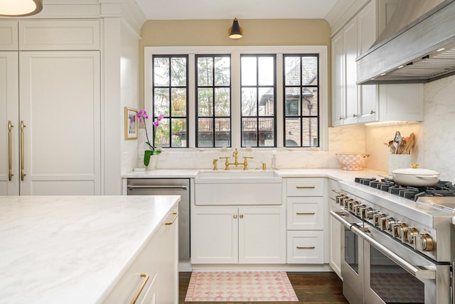 kitchen featuring range with two ovens, light stone counters, premium range hood, a sink, and white cabinets