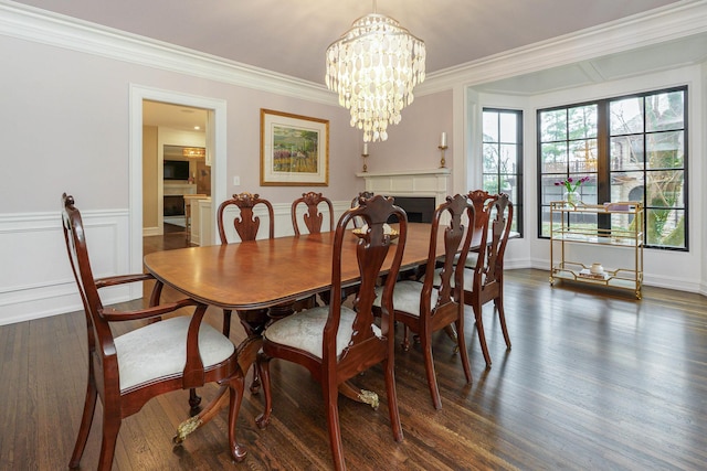 dining space with dark wood finished floors, wainscoting, crown molding, a fireplace, and a notable chandelier