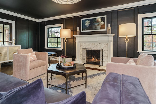 living room featuring a premium fireplace, ornamental molding, a decorative wall, and wood finished floors