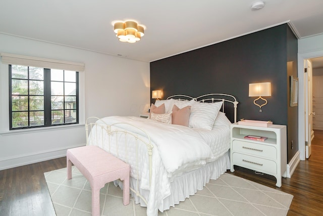 bedroom with an accent wall, baseboards, and wood finished floors