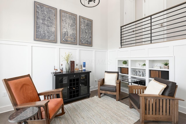 sitting room with wood finished floors, a towering ceiling, and a decorative wall