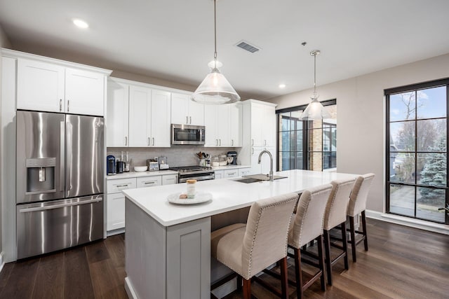 kitchen featuring stainless steel appliances, a sink, light countertops, dark wood-style floors, and an island with sink