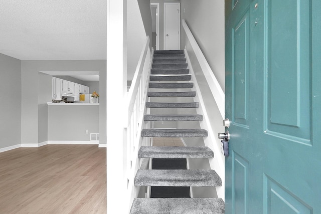 stairs featuring baseboards, a textured ceiling, visible vents, and wood finished floors