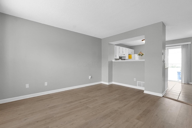 empty room with a textured ceiling, dark wood-type flooring, visible vents, and baseboards