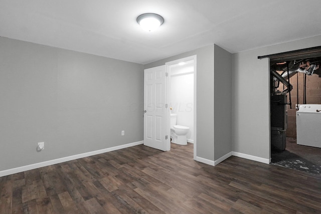 unfurnished bedroom featuring ensuite bathroom, wood finished floors, washer / dryer, and baseboards