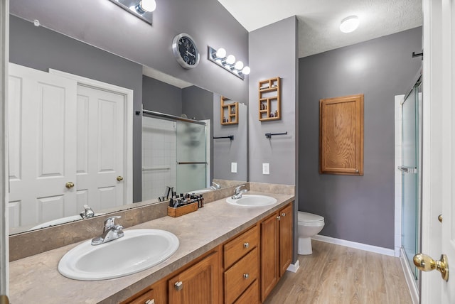 full bathroom featuring wood finished floors, a sink, toilet, and an enclosed shower