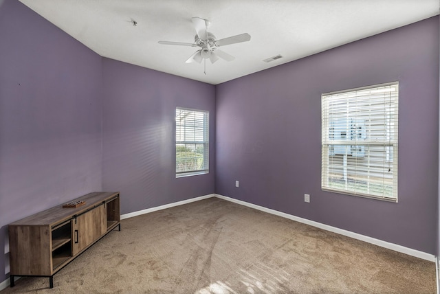 empty room with light carpet, a ceiling fan, visible vents, and baseboards