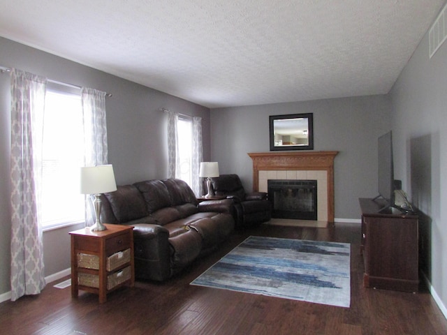 living room with a tile fireplace, visible vents, a wealth of natural light, and wood finished floors