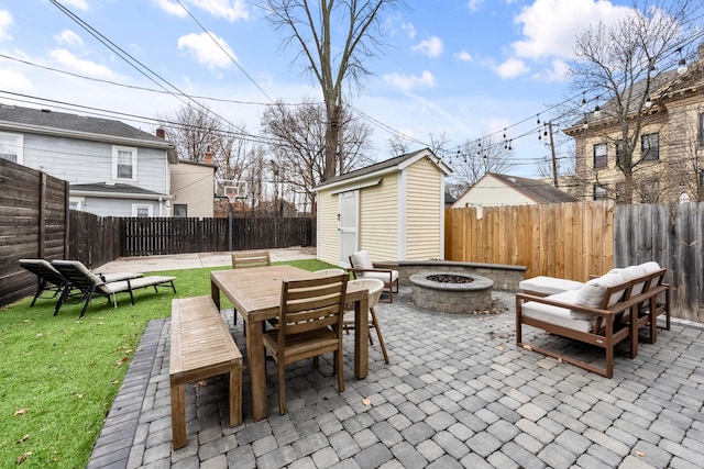 view of patio / terrace with a fire pit, a fenced backyard, a storage unit, outdoor dining area, and an outdoor structure