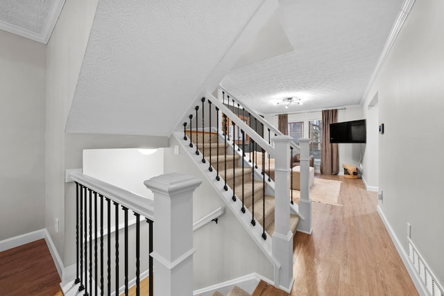 staircase featuring crown molding, baseboards, and wood finished floors